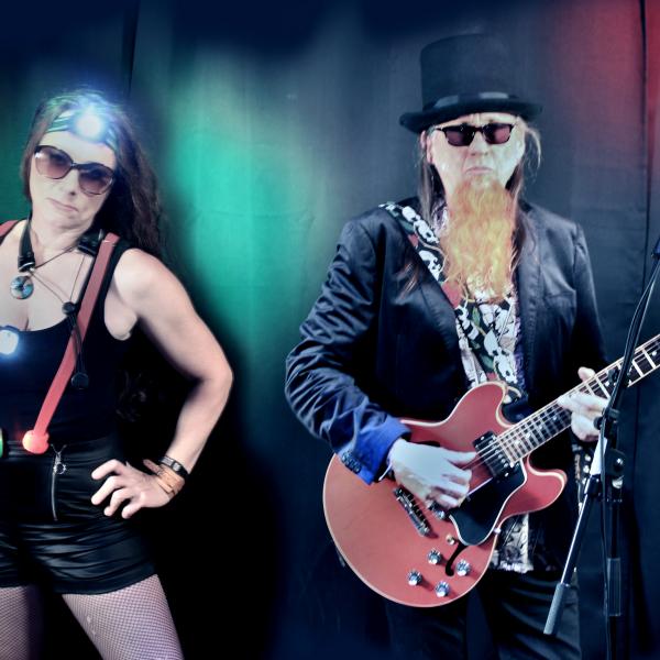 Herrbart & Fraulicht stehen auf der Bühne mit Gitarre, Lichtern und Sonnenbrillen